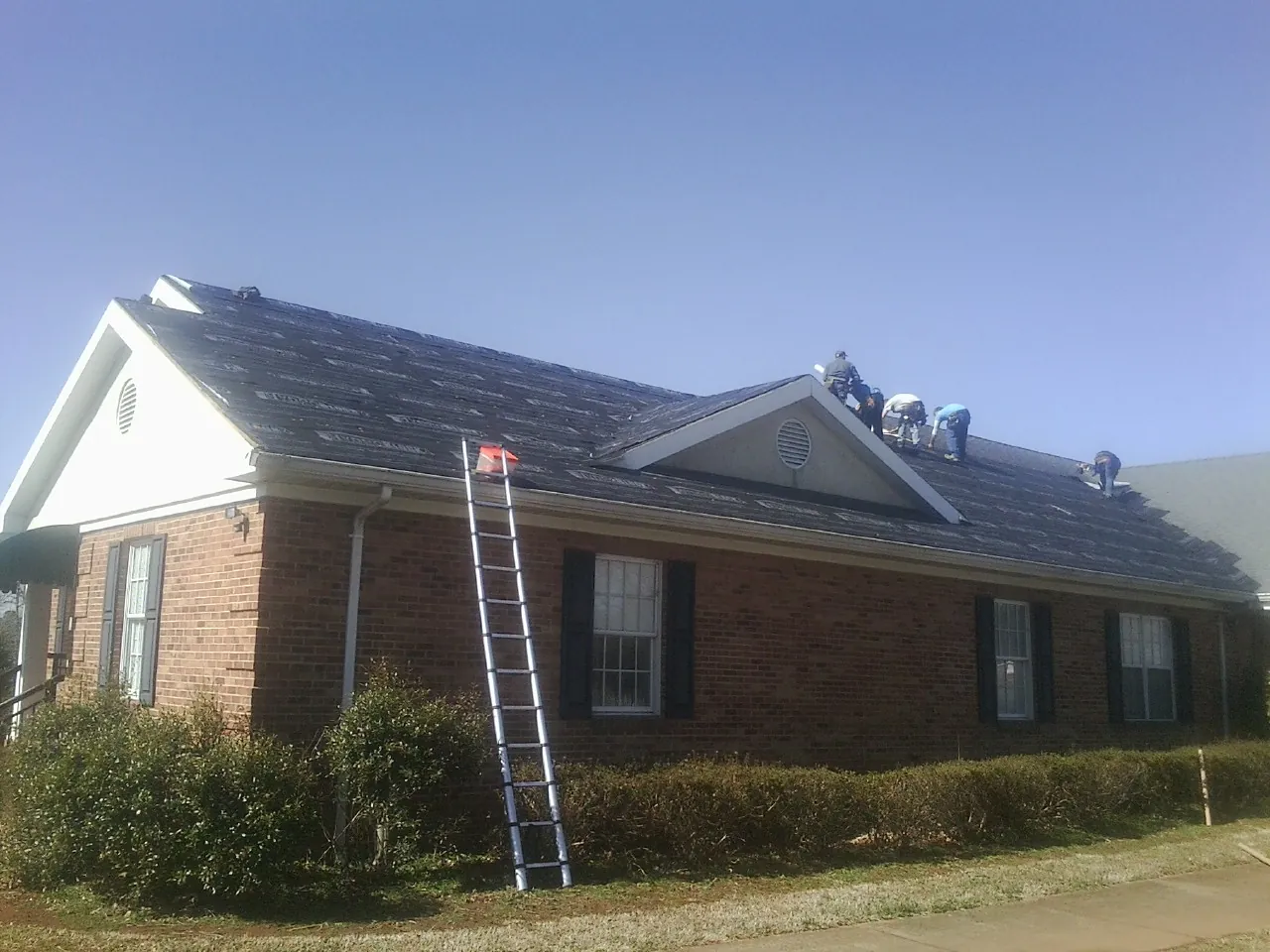 Crew tearing shingles off a brick ranch roof with a ladder set — Emergency Roof Repair work by our crew in Amenia