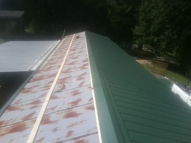 Old rusted panels beside newly installed green metal roofing — Wind Damage Roof Repair by Roofing Brothers in Amenia