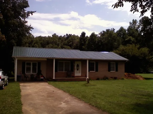 Dark green metal roof on a brick ranch with a covered porch in Amenia