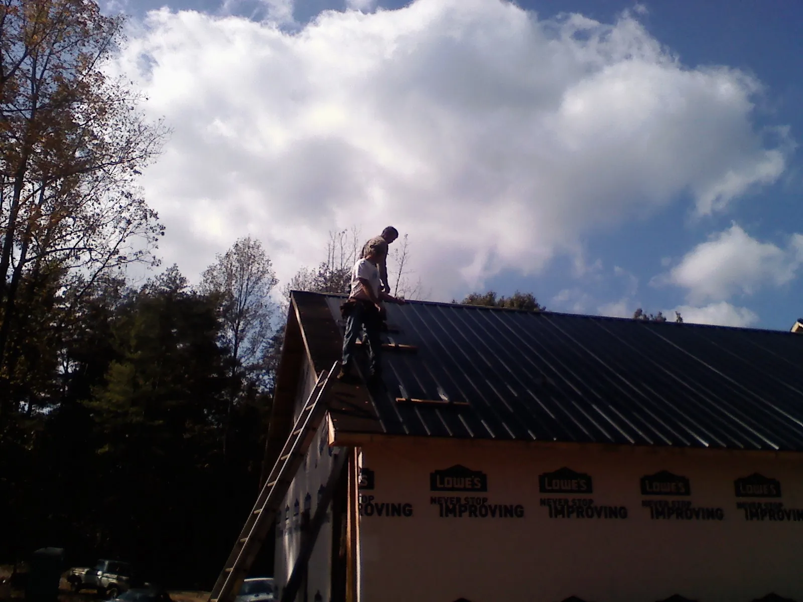 Roofer fastening dark metal panels high against a cloudy sky, from a Roof Inspection job in Amenia