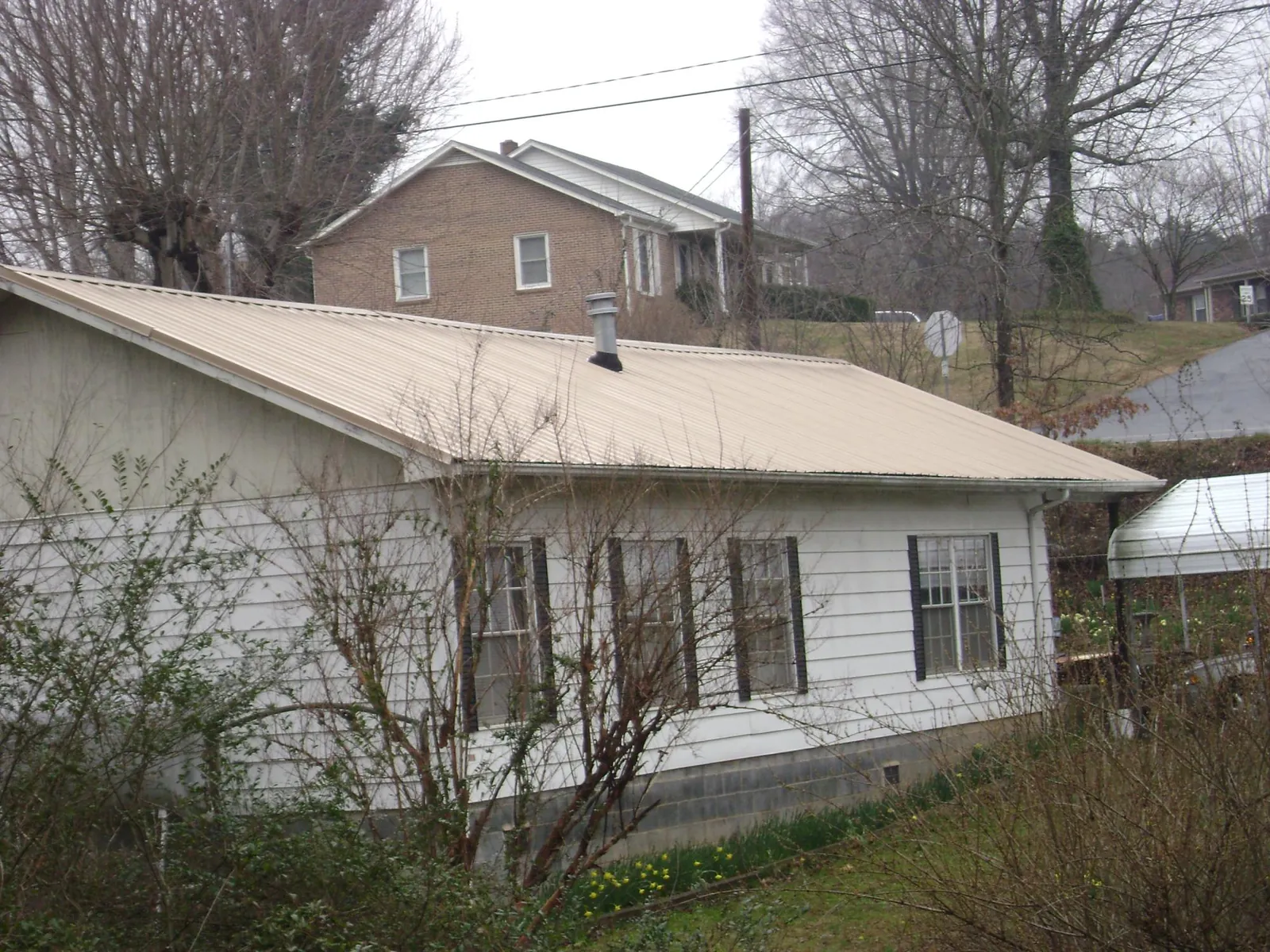 Tan metal roof on a white sided house set into a hillside — Commercial Roofing by Roofing Brothers in Amenia