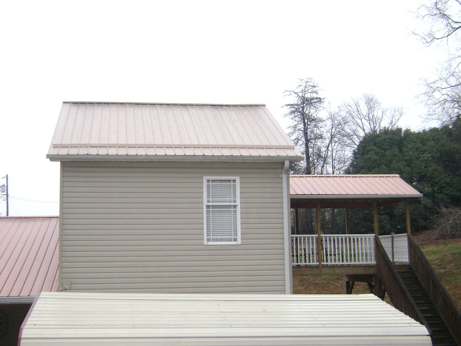 Tan metal roofs on a two story addition and attached porch, from a Roof Replacement job in Amenia